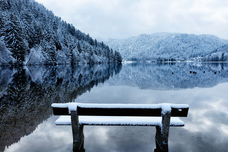 Bench by the Longemer Lake in the Vosges mountains, Xonrupt-Longemer, Lorraine, France. Winter landscape with white snowy trees reflected in water.の写真素材