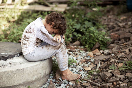 Dirty homeless boy looks through eyes full of tears