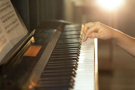 female hands touch the piano keys, play a melody, in the rays of the setting sun
