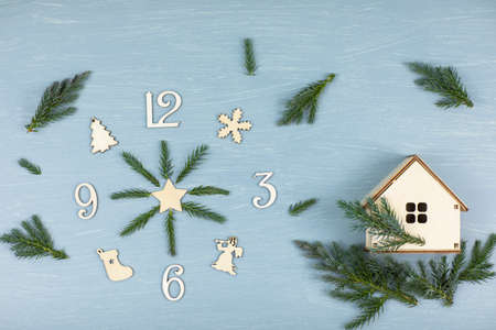 clock made of wooden numerals with spruce branches on a blue background, next to a wooden house. High quality photoの写真素材