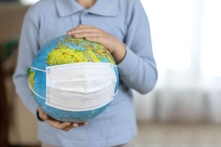 globe in a mask in the hands of a child, a concept of a virus on the planet. High quality photo