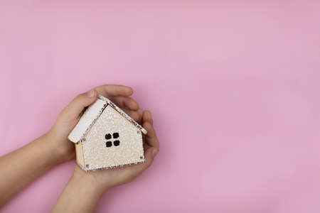 A small wooden house in the hands on a pink background, the concept of construction. High quality photoの写真素材