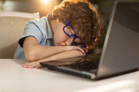 a boy wearing glasses at home in the rays of the sunset, fell asleep near the laptop. High quality...