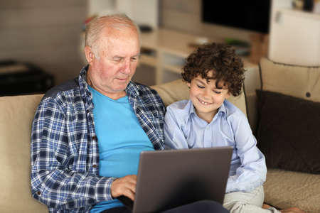 Grandfather and grandson study on the computer at homeの写真素材