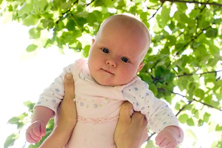 Mother holding her child against sunny leaves at summer gardenの写真素材