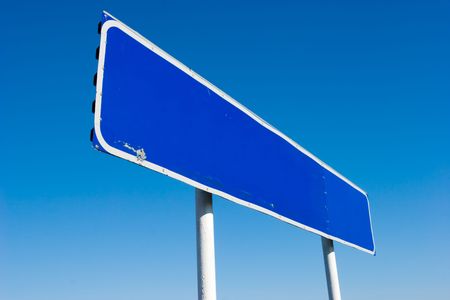 Old grungy blank signpost against blue skyの写真素材