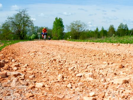 Traveling cyclists on dirt road, focus on the roadの写真素材