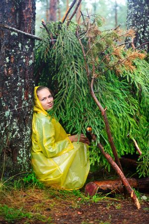 Young woman wearing yellow  raincoat sitting in a shelter of branches