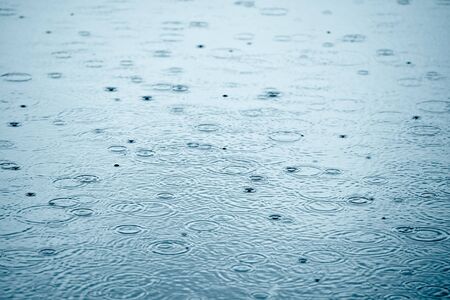 Rain drops rippling in a puddle with blue sky reflectionの写真素材