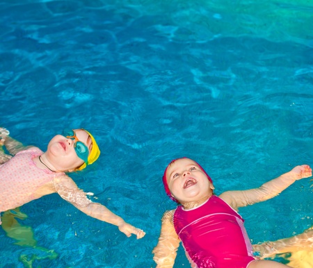 Two happy little girls learning to swim in a poolの写真素材