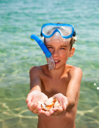 Boy wearing snorkeling gear showing seashellsの写真素材