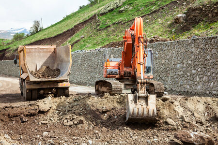 Excavator loading dirt into a truck at road construstion site