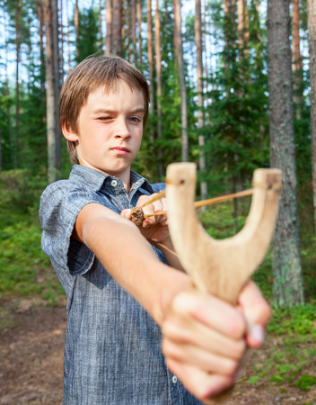 Boy aiming wooden slingshot outdoors