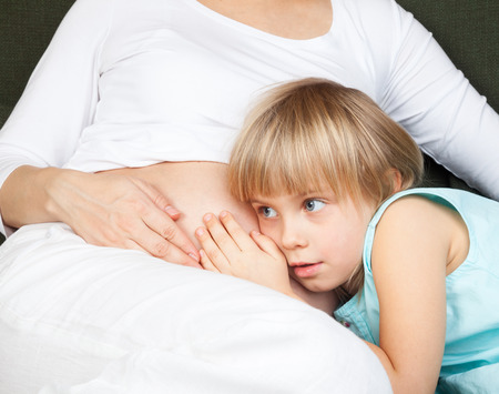 Little girl listening to her pregnant mother's bellyの写真素材