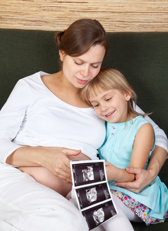 Little girl  with her pregnant mother looking at ultrasound scan of a fetus