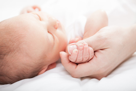 Newborn baby holding mother's thumbの写真素材