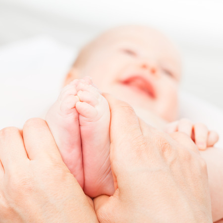 Close-up shot of three month baby girl receiving foot massage from a female massage therapist. Camera is focused on infant's feet. Happy face is blurred in background.の写真素材
