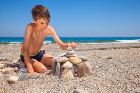 Boy building pebble castle on a beachの写真素材