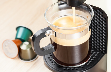 Single-serving coffee machine dispenses  espresso in a glass cup  with coffee capsules in backgroundのeditorial素材