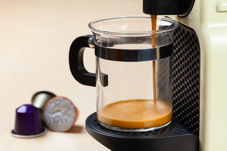 Single-serving coffee machine dispenses  espresso in a glass cup  with coffee capsules in backgroundのeditorial素材