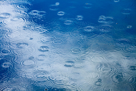 Rain drops rippling in a puddle with blue sky reflection