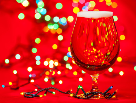Full snifter glass of pale lager of beer with christmas lights on red backgroundの写真素材