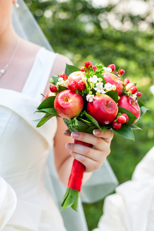 Bride holding wedding bouquet made of green leaves white flowers red apples and berriesの写真素材