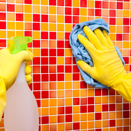 Person doing chores in bathroom at home cleaning red orange tiled wall with spray detergent and blue microfiber towelの写真素材