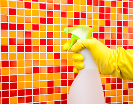 Person doing chores in bathroom at home cleaning red orange tiled wall with spray detergent