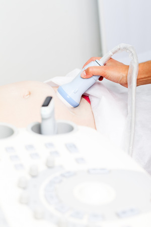 Close-up shot of sonographer scanning young pregnant woman's belly with ultrasonic transducer doing obstetric ultrasonographyの写真素材
