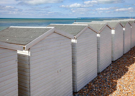 Row of white wooden cabins on shingle beach at popular seaside resort Bexhill-on-Sea in East Sussex South East England UKの写真素材