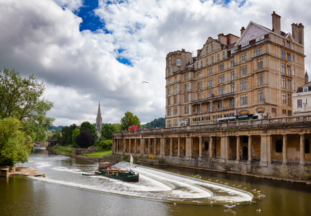 BATH, UK - JUN 11, 2013: View of The Empire Hotel near Pulteney Bridge and the Pulteney weir on the River Avon with the Parade Gardens park in backgroundのeditorial素材