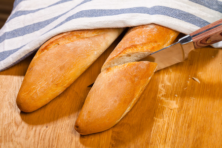 Cutting sreshly baked artisanal baguette  (french bread) with kiychen knife on wooden table