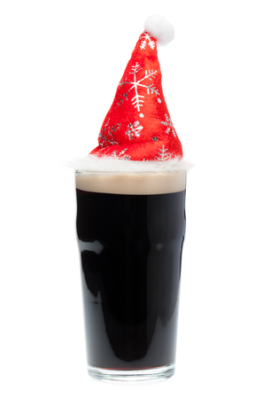 Nonik pint glass of dark beer or stout ale with red christmas or santa claus hat on white backgroundの写真素材