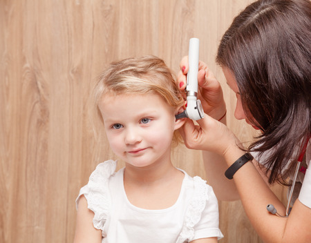Female pediatrician examines little girl's ear. Doctor using a otoscope or auriscope to check ear canal and eardrum membrane. Child ENT check conceptの写真素材