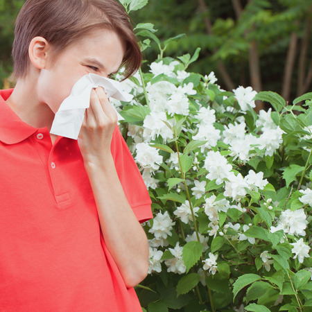 Teenager boy with seasonal influenza blowing his nose on a tissue in a spring garden -  seasonal infection conceptの写真素材