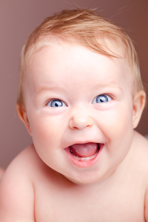 Head and shoulders portrait of cute blue-eyed baby girl looking at camera and laughing  on a coral color background - happy babyhood or childhood conceptの写真素材