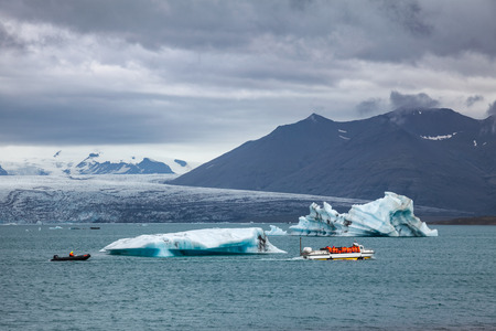 Tourists wearing life jackets taking a boat tour on amphibious vehicle passing iceberg at the...