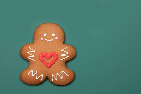 Christmas Gingerbread man sugar cookie in humanoid shape with red heart icing decoration on green...