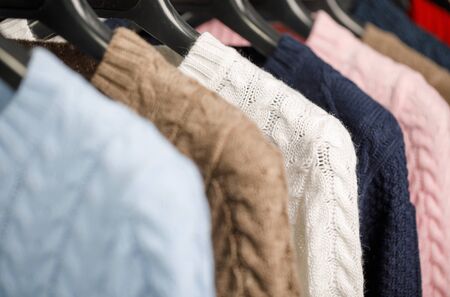 Various cable knit sweaters or pullovers on hanger rack in a clothes store or at a wardrobe,...