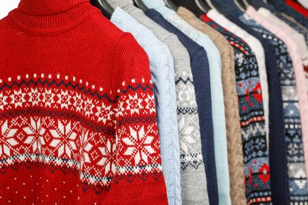 Various knitted turtleneck sweaters and pullovers with norwegian ornament on hanger rack in a clothes store or at a wardrobe, selective focusの写真素材