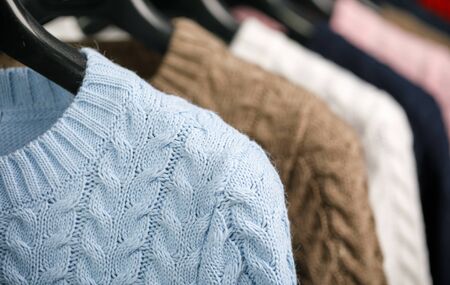 Various cable knit sweaters or pullovers on hanger rack in a clothes store or at a wardrobe,...