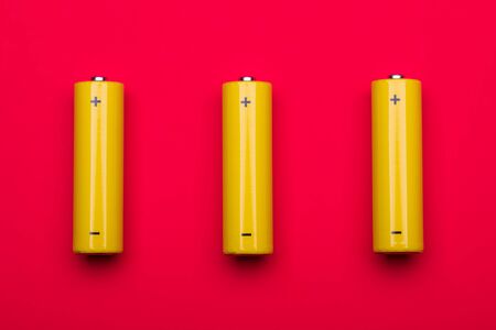 Top view of 3 yellow AA alkaline or rechargeable NiMH batteries on red backgroundの写真素材