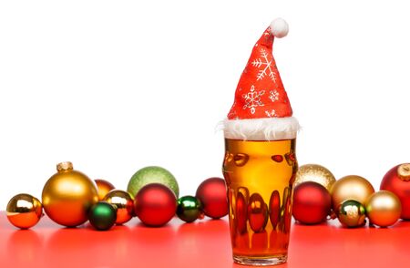 Full pint glass of lager beer or ale with Santa Claus red hat and christmas baubles on red isolated on white backgroundの写真素材