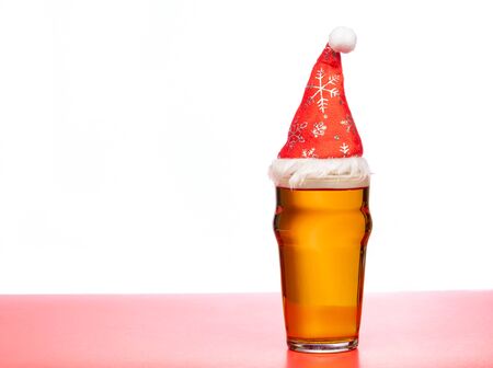 Full pint glass of lager beer or ale with Santa Claus red hat on red isolated on white backgroundの写真素材