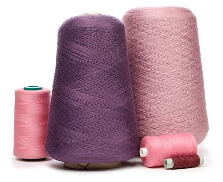 Group of cones and spools of pink purple and violet synthetic or cotton threads on white background...