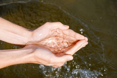 Woman taking raw unfiltered water from a natural source by cupped handsの写真素材