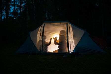 Silhouettes of children playing in camping tent at night making shadow puppets with flashlight enjoying summer holidaysの写真素材