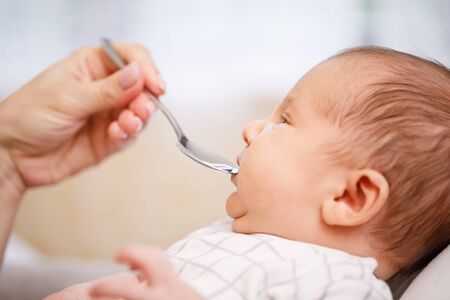 Mother feeding newborn baby with vitamin or liquid medicine using dose spoonの写真素材