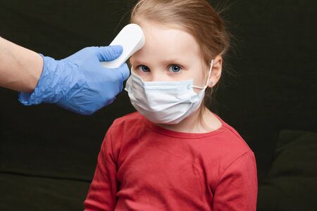 Pediatrician or doctor checks little girl's body temperature using infrared forehead thermometer (thermometer gun) for virus symptom - epidemic coronavirus screening conceptの写真素材